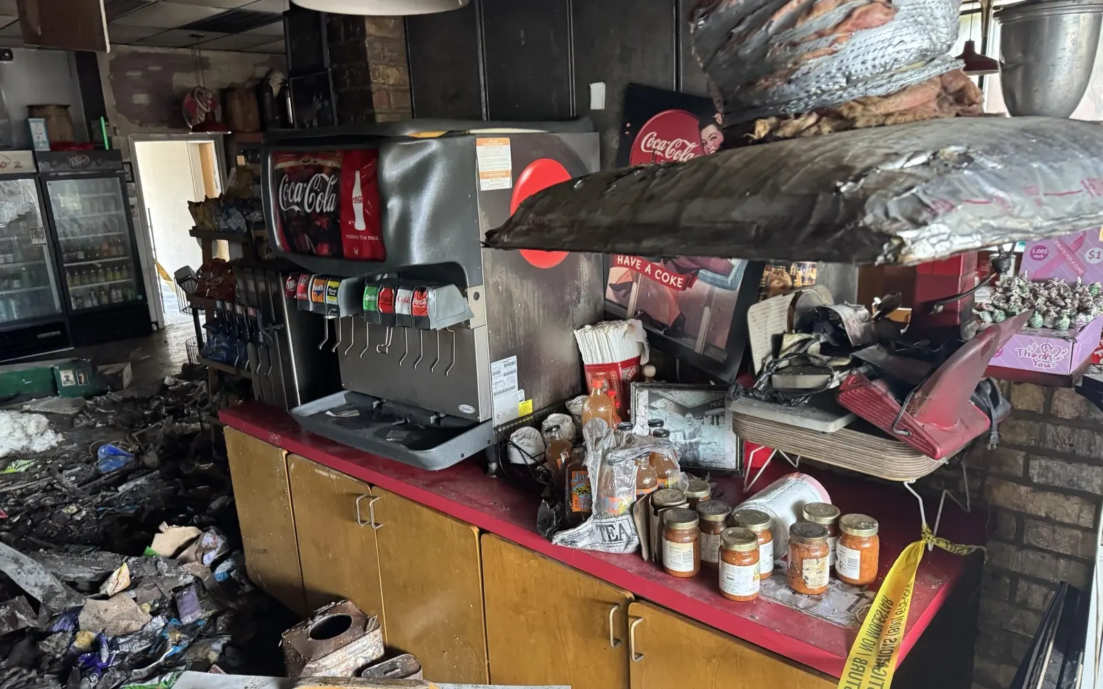 Burned retail counter, coolers and fixtures inside a commercial storefront after a fire