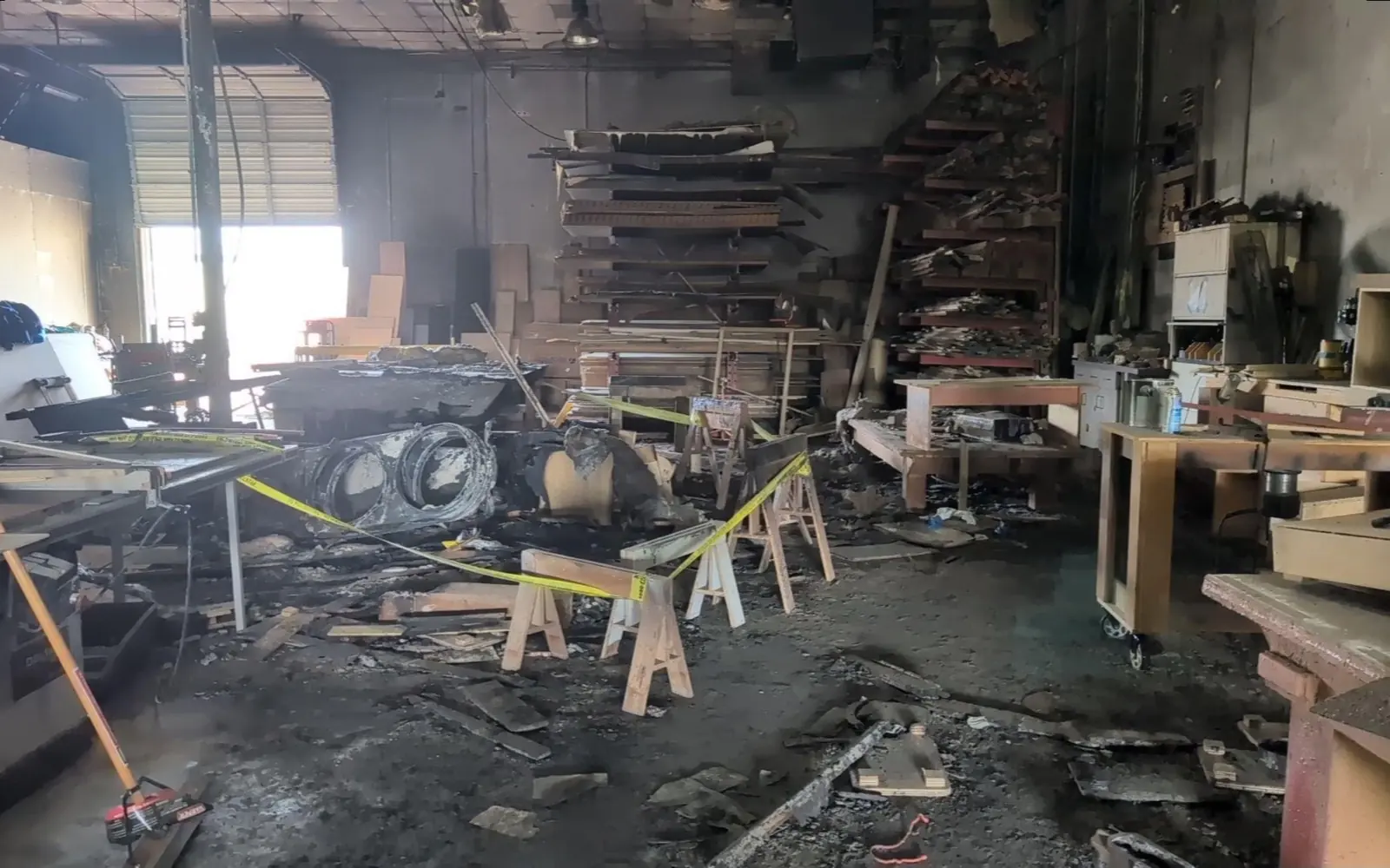 Fire-damaged manufacturing floor with machinery, workbenches and stock behind caution tape